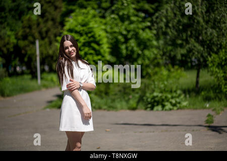Young Smiling Brunette Woman In The Park Touching Her Right Hand With Her Left Hand. Stock Photo