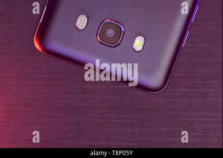 A fragment of the cell phone case in black with pink and purple backlight. The phone is on black tech ribbed surface camera pink up lighting. Stock Photo