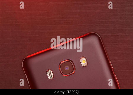 A fragment of the cell phone case in black with red backlight. The phone lies on the black technological ribbed surface of the camera up with red back Stock Photo