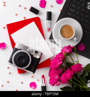 Bouquet of roses, cup of coffee, laptop, camera, notepad and lipstick on white table. Stock Photo