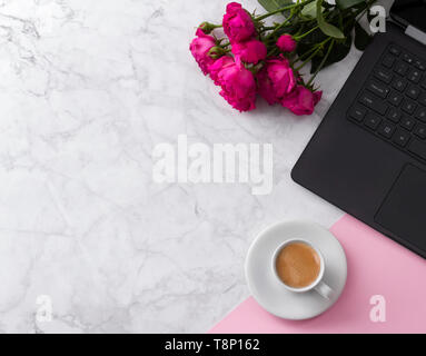 Feminine workspace with laptop computer, bouquet of roses and coffee on a marble table.  Stock Photo