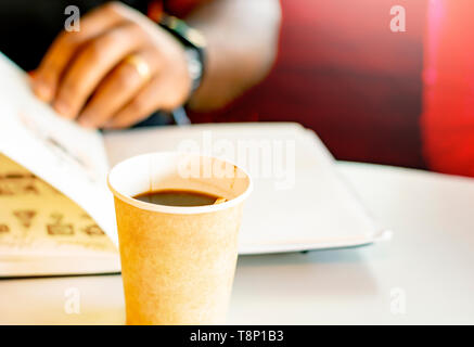 A mug of coffee with a black man reading a book in the background. Taking a break with a coffee Stock Photo