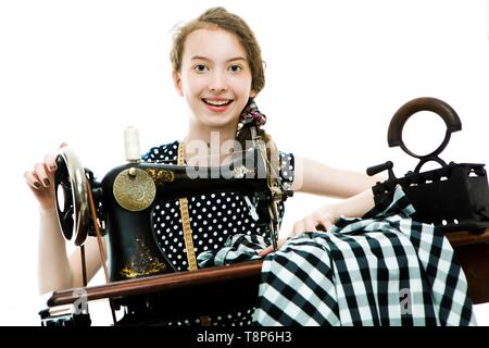 Teenaged girl dressmaker using antique sewing manual machine - vintage tailor's tools scissors and coal iron - concept on white background Stock Photo