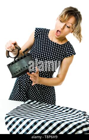 Attractive housewife in pin up style feels pain from hot vintage coal metal iron during ironing - high temperature tool - concept on white background Stock Photo