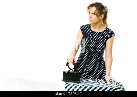 Attractive housewife ironing checkered dress using vintage coal metal ironing tool - concept on white background Stock Photo
