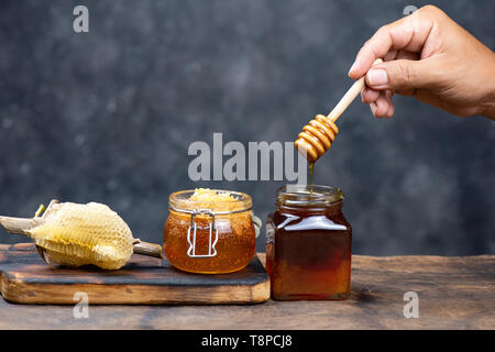 hand holding wooden honey dipper, honey spoon on top of glass of tea  on wood table Stock Photo