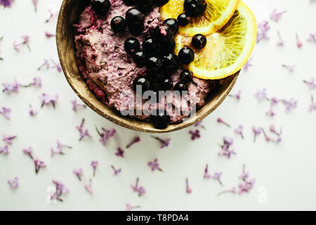 healthy smoothie bowl breakfast in a coconut shell with lilac flowers on white background Stock Photo