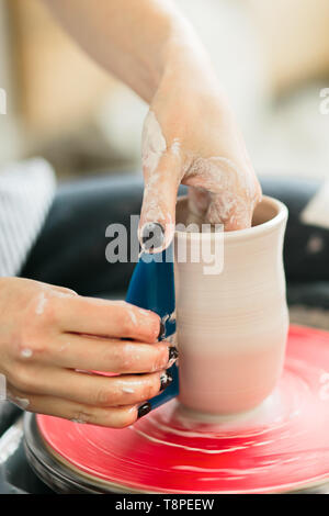 Women working on the potter's wheel. Hands sculpts a cup from clay pot. Workshop on modeling on the potter's wheel. Stock Photo