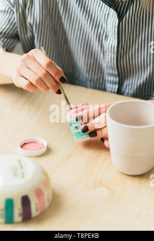 the pottery woman holds in hands a mug to paint the ornament, handmade ceramic Stock Photo