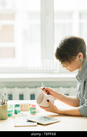 the pottery woman holds in hands a mug to paint the ornament, handmade ceramic Stock Photo
