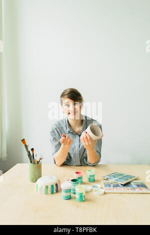 the pottery woman holds in hands a mug to paint the ornament, handmade ceramic Stock Photo
