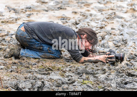 Female photographer lying in mud photographing at the Maldon Mud Race in the River Blackwater, Maldon, Essex, UK. Getting the shot
