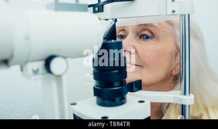 Senior woman doing eye test with eye equipment Stock Photo