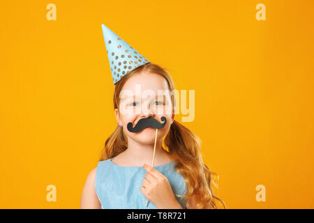 Happy father's day. Funny little girl with fake mustache on yellow background. Family concept. Stock Photo