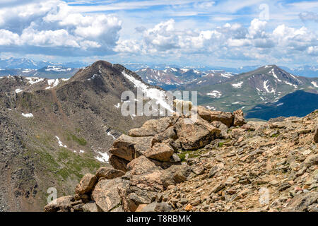 Mountain Goat on Cliff - A mountain goat standing on a steep rocky cliff in front of Mt. Bierstadt and rolling front range of Rocky Mountains, CO, US. Stock Photo
