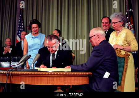President Lyndon B. Johnson signing the Medicare Bill at the Harry S. Truman Library in Independence, Missouri. Former president Harry S. Truman is seated at the table with President Johnson. The following are in the background (from left to right): Senator Edward V. Long, an unidentified man, Lady Bird Johnson, Senator Mike Mansfield, Vice President Hubert Humphrey, and Bess Truman. July 30,1965 Stock Photo