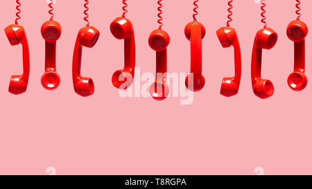 Various views of old red telephone receivers hanging on pink background with texting space, waiting for phone call, customer service concept, vintage  Stock Photo