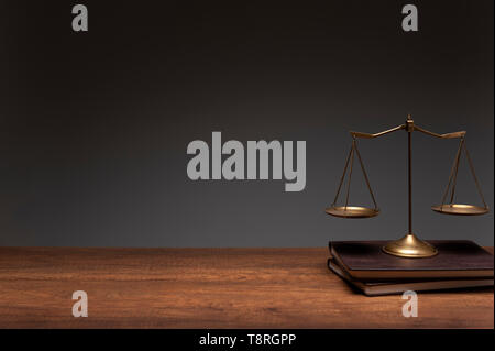 Gold brass balance scale placed on the vintage books and wood table with gray background, legal law concept. Stock Photo