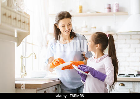 Helping hand. Cute teenage girl helping her mother in washing dishes at family kitchen Stock Photo