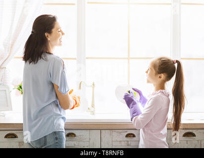 Daughter helping mom in washing dishes in kitchen Stock Photo
