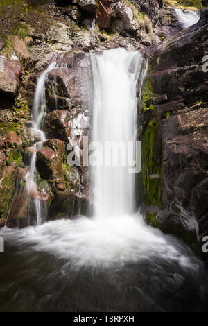 Unique, close up view of a scenic waterfall during spring streaming down the red, wet cliff with vibrant green moss Stock Photo
