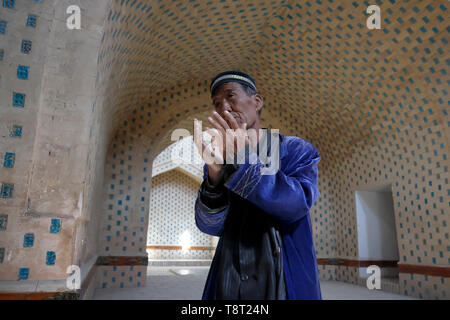 An elderly Uzbek man prays inside the restored Mausoleum of Mazlum Khan Slu which is also known as Mazlumkhon-Sulu, lined with bright blue tiles dating back to the 14th century in Mizdakhan necropolis, ancient cemetery, considered one of the most important Zoroastrian sites in Central Asia located on south of the city Khodjeyli in the autonomous Republic of Karakalpakstan within Uzbekistan Stock Photo