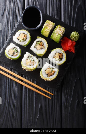 Japanese rolls wrapped in avocado with omelet, sesame and cucumber closeup on a plate on the table. Vertical top view from above Stock Photo