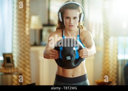 young sports woman in headphones in fitness clothes at modern home doing functional training exercises. Stock Photo