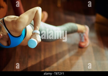 Closeup on young woman in sport clothes with blue dumbbell workout in the modern house. Stock Photo