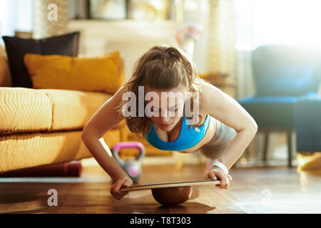 fit woman in fitness clothes in the modern living room doing pushups using balance board. Stock Photo