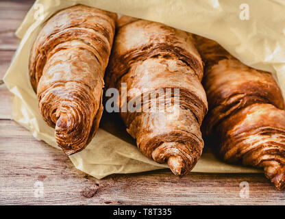 Three delicious croissants wrapped in baking paper on wooden table. Close-up. Stock Photo