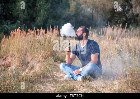 Bearded man smokes electronic cigarette exhales smoke. Alternative to smoking. Stock Photo