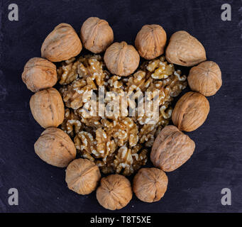 Walnuts, with and without shell, heart shaped, on black surface Stock Photo