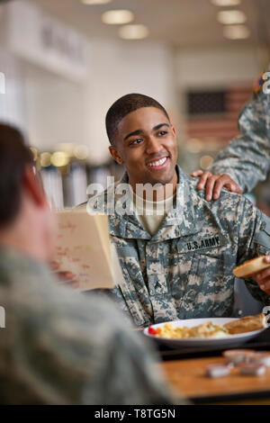Young soldier smiles happily as he reads a letter over breakfast in the army mess hall. Stock Photo
