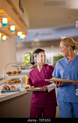 Two young nurses smile and chat together as they get their lunch from the hospital canteen. Stock Photo