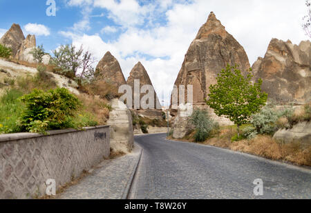 A winding road from paving stones passes near the stone cone houses in the ancient rocks of Goreme, Kappadoki. Rural landscape in the rural way of lif Stock Photo