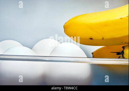 Banana Fingers and Four White Eggs in Open Refrigerator Door Plastic Container. Weight Loss Diet, Healthy Organic Food and Lifestyle Concept. Stock Photo