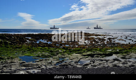 Rocky beach at low tide and oil  platforms in the bay, coast of Las Palmas, Gran Canaria Stock Photo