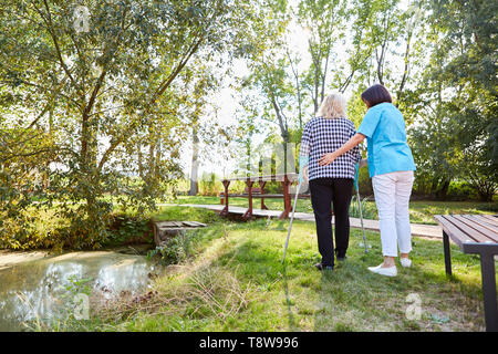 Nurse helps patient with crutches while learning to walk in the park