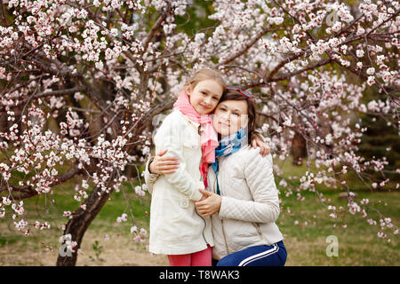 Happy young woman with her little baby girl. Mother walking with daughter on a spring day. Parent and kid enjoying cherry blossom season. Baby wearing Stock Photo