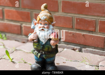 The figure of a garden gnome against a red brick wall. Close-up. Copy space. Stock Photo