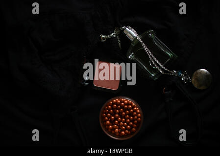pendant necklace, blusher, bronzer and a perfume bottle on a black background