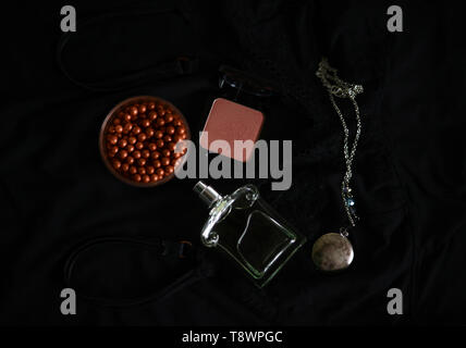 pendant necklace, blusher, bronzer and a perfume bottle on a black background