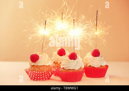 Delicious birthday cupcakes with sparklers on color table Stock Photo