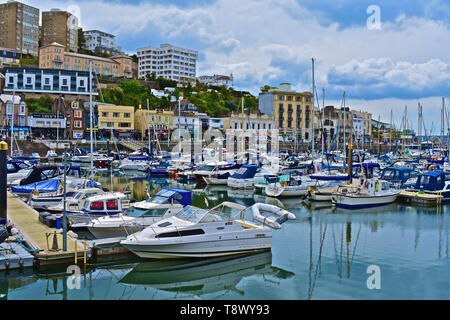 A street view across the inner harbour/ marina at Torquay with yachts at moorings. Calm still waters with reflections of boats and buildings. Stock Photo