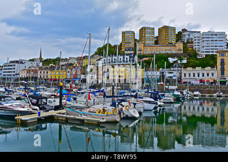 A street view across the inner harbour/ marina at Torquay with yachts at moorings. Calm still waters with reflections of boats and buildings. Stock Photo