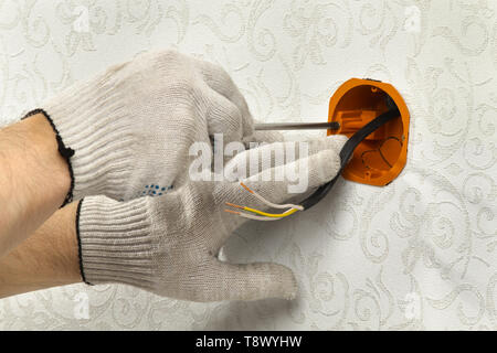 hands of an electrician fasten the socket box to the wall to place the electrical outlet Stock Photo