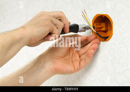 hands of an electrician fasten the socket box to the wall Stock Photo