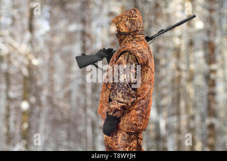 hunter in autumn camouflage with a gun on his shoulder in the winter forest Stock Photo