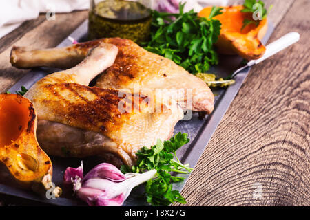 Grilled chicken legs served with roasted pumpkin, pesto sauce and fresh parsley on rustic wooden table, meat and vegetables roast dinner Stock Photo